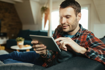 Young smiling man using touchpad while relaxing at home.
