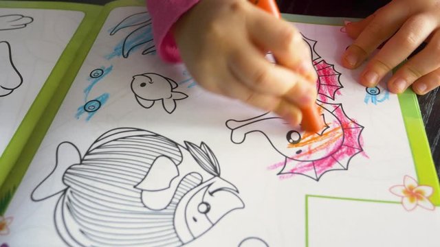 A three-year-old child paints a book with colored crayons