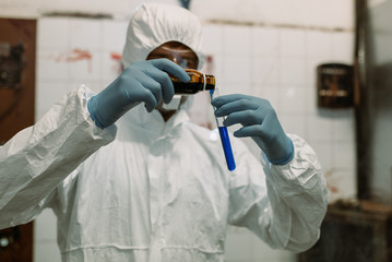 Scientist doctor biologist in hazmat suit and protective respiratory mask working in laboratory with test tubes searching vaccine against Coronavirus COVID-19