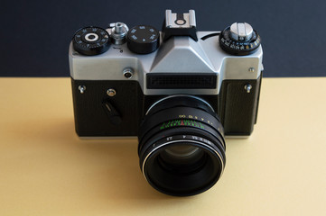 Vintage film photo camera on the dark and yellow background. Metal silver and plastic black frame with lens.