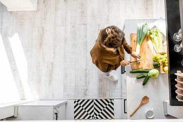 Woman cooking some food, cutting fresh ingredients on the cutting board on the kitchen, view from above