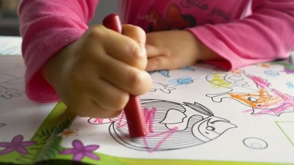 A three-year-old child paints a book with colored crayons