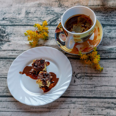 The delicious traditional Italian dessert called mimosa covered in liquid chocolate with a cup of barley coffee and yellow sedum flowers