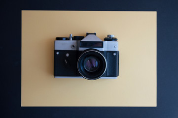 Fototapeta premium View from the top on vintage film photo camera on the dark and yellow background. Metal silver and plastic black frame with lens