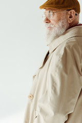 Side view of stylish man in trench coat and beret on grey background