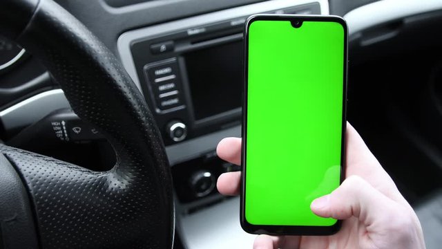 In the modern new car young man hand using smartphone , mobile phone with vertical green screen indooors.Internet Social Networks Browsing.Chroma key.Close up