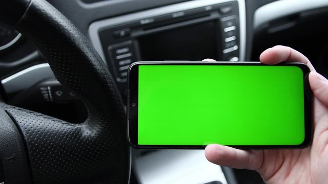 In the modern new car young man hand using smartphone , mobile phone with vertical green screen indooors.Internet Social Networks Browsing.Chroma key.Close up