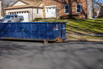 Long blue dumpster on a street by a curb near residential home