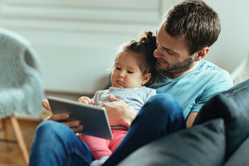 Young father with small daughter watching something on digital tablet at home.