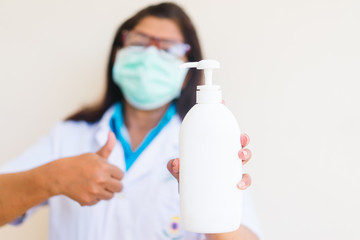 Obraz premium Doctor wearing surgical face mask holding showing alcohol gel pump bottle. washing hands with alcohol gel or antibacterial soap sanitizer.Covid-19 or Coronavirus concept.