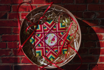 Portuguese star mandala made of multi-colored threads and beads in a beautiful box on a background of a red brick wall