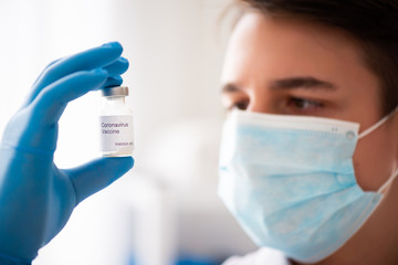 Vaccine bottle in male hand close up, doctor in medical mask. Concept of vaccination, Covid-19...