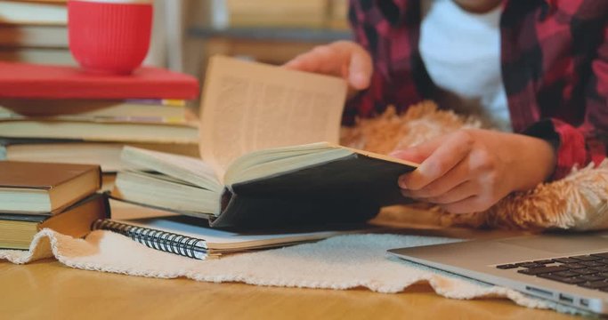 Young woman student studying at home with many books and laptop