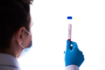 Test tube in male hand close up, doctor in medical mask holding vial with red liquid. Concept blood sample, coronavirus diagnostic, medical research