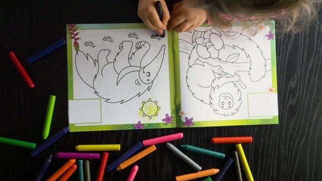 A three-year-old child paints a book with colored crayons