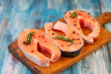 Three raw salmon steaks on a wooden cutting board prepared for cooking, top view