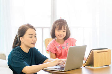 Fototapeta na wymiar Covid-19 Coronavirus and Learning from home, Home school kid concept.Little asian girl study with online learning and asian mother work from home with laptop.Quarantine and Social distancing concept.