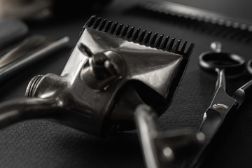 On a black surface are old barber tools. vintage manual hair clipper, razor, comb, shaving brush, hairdressing scissors. black monochrome. horizontal