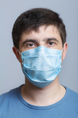 Portrait of young doctor in surgical mask and blue uniform confidently looking on a gray studio background, concept of medicine and health