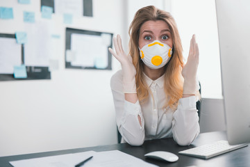 young blond woman manager in medical protection mask and gloves looks panicky while working in...