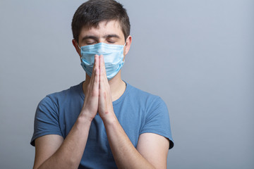 young man in a protective medical mask praying to God for help and support in difficult times for mankind, doctor on studio backgroung, concept life and religion