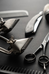 On a black surface are old barber tools. two vintage manual hair clipper, comb, razor, shaving brush, hairdressing scissors. black monochrome. vertical