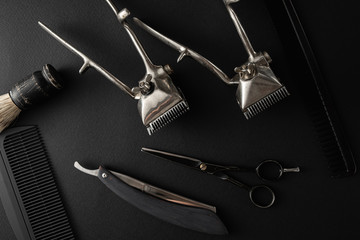 On a black surface are old barber tools. two vintage manual hair clipper, comb, razor, shaving brush, hairdressing scissors. black monochrome. horizontal orientation.