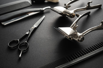 On a black surface are old barber tools. two vintage manual hair clipper, comb, razor, shaving brush, hairdressing scissors. black monochrome.