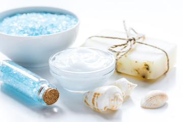 blue bath salt, body cream and shells for spa on white table background