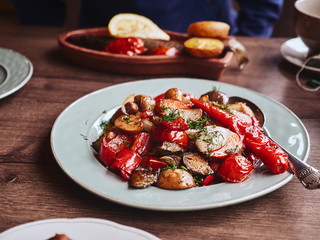 Traditional Georgian vegetable salad mushrooms, pepper, onions and dill on white rustic plate on wooden table