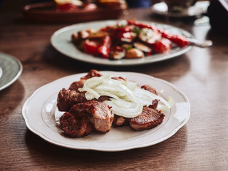 Traditional Georgian grilled pork with fresh onion on white rustic plate on wooden table