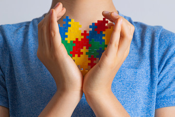 World autism awareness day concept. Child hands holding colorful puzzle heart against him