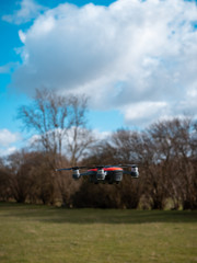 Obraz na płótnie Canvas Small red drone flying low. Sky and trees background. Spinning propellers. Unmanned aircraft system. UAV 