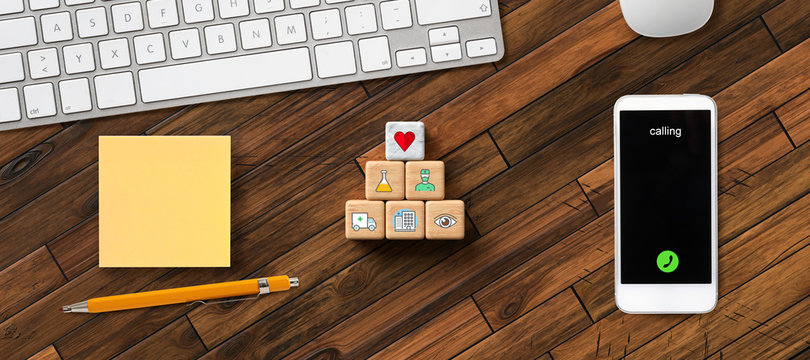 cubes with health symbols surrounded by smartphone, keyboard, notepad and a pen on wooden background