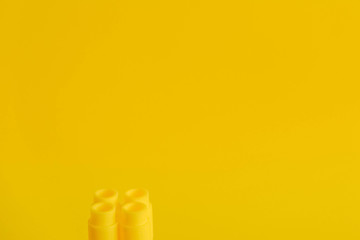 Yellow plastic building block on yellow background. Background of plastic detail building block. Part of bright small spare part for toys. Copy, empty space for text