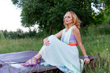        The girl in the dress sits leaning on one hand.