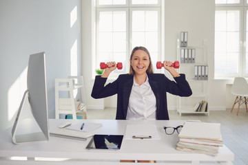 Businesswoman is doing exercises with dumbbells in the office during the break.