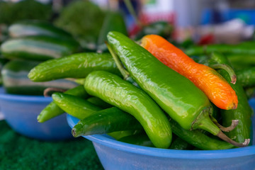 A closeup of a blue bowl of long hot green Chile peppers with the exception of one Mexican orange one. The fresh organic hot chili peppers still have their stems. The fresh produce is a raw plant. 