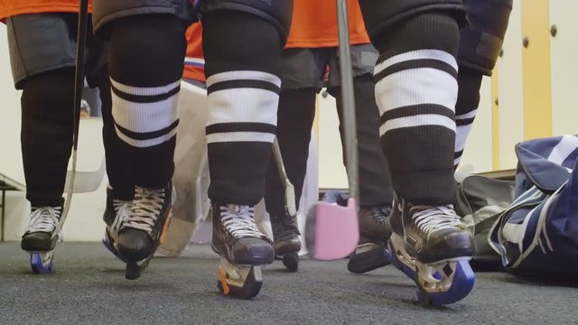 Close up of few unrecognizable hockey players wearing hockey equipment and skates going along dressing room