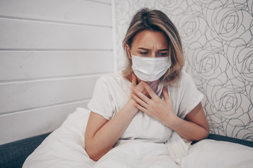 Young woman coughing in arms sick of coronavirus viral infection spreading corona virus covering mouth and nose. Painful cough ill patient lying in bed at home quarantine isolation. First symptoms