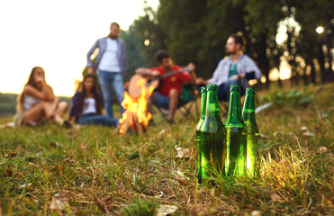Beer bottles on the background of friends by the bonfire on a picnic.