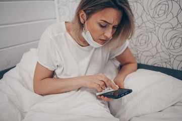 Woman in face protective mask lying in bed during coronavirus isolation home quarantine cleaning...
