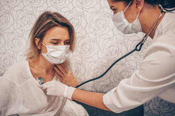 Doctor nurse in protective face mask listening to breath with a stethoscope suspecting Coronavirus...