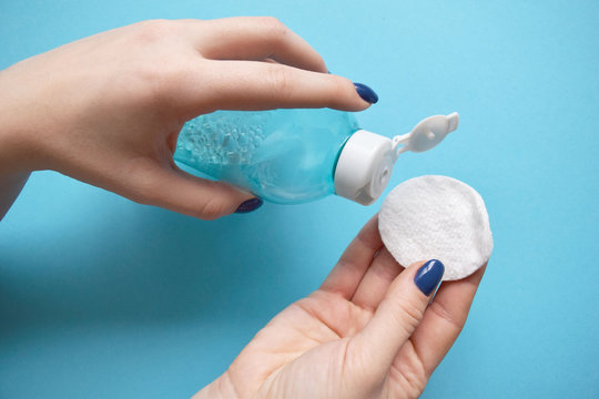 Woman's Hand Hold Cotton Pad And Tonic On A Blue Background. Beauty Concept, Clean Cosmetics.