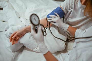 Unrecognizable doctor nurse in medical gloves measures blood pressure with a sphygmomanometer. Coronavirus (COVID-19). First symptoms. Woman sick of flu viral infection in home isolation quarantine