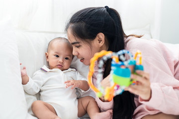 Asian cute baby and young mother playing toy on bed at home. Baby smiles and looks at toy feeling enjoy and happy with mom. Infant kid toy for education. Parent and baby skill development concept.