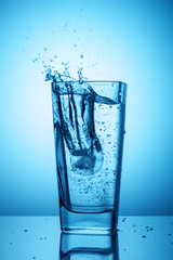 Splashes of clean transparent drinking water in a glass on a blue background