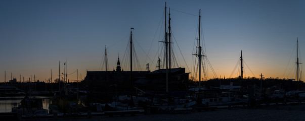 Fototapeta na wymiar Morning skyline view at sunrise over the district Djurgården with boats, ice and towers in orange back light in Stockholm.
