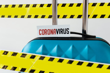 close up view of blue suitcase with coronavirus card in yellow and black hazard warning safety tape isolated on white