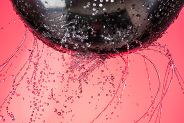 many trickles and drops of water through holes in a meialic colander on a red background